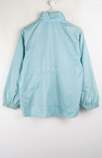 A light blue Nike windbreaker jacket hanging on a white hanger against a plain white wall, showing the back view with a small white Nike logo.