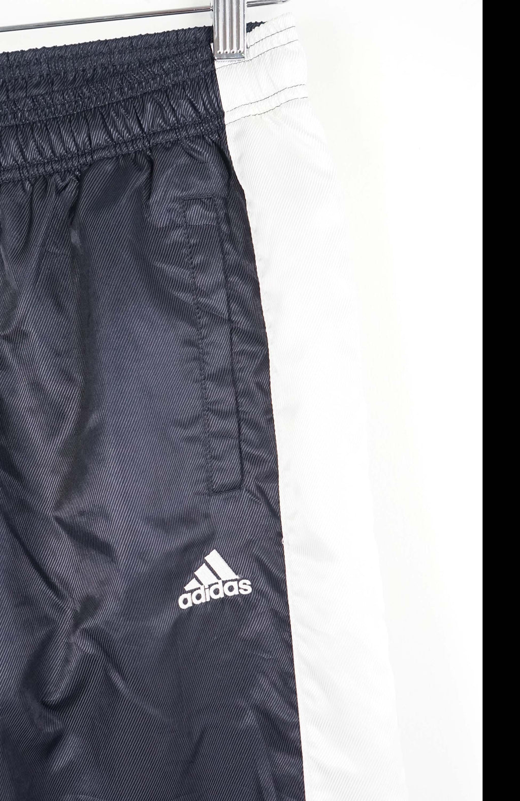 Black Adidas tracksuit pants hanging on a white background