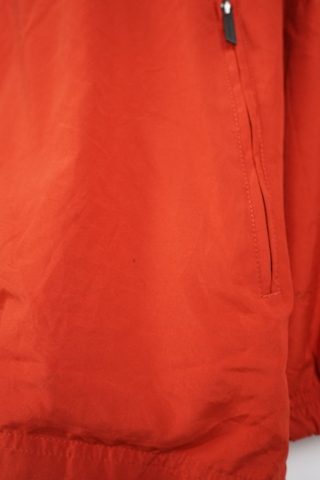 Red jacket with white stripes on sleeves hanging on a white background