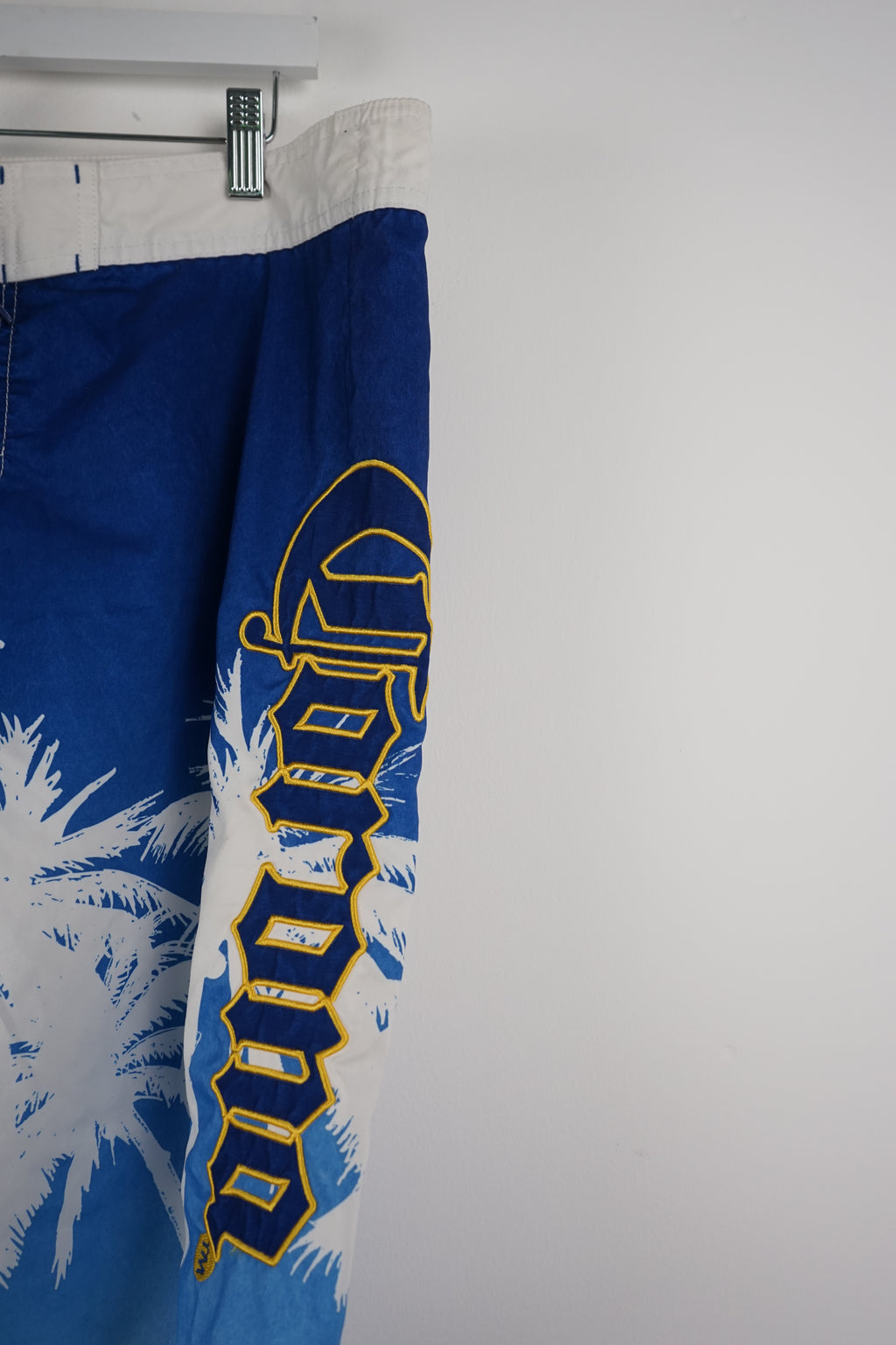 Blue board shorts with palm tree design and brand logo on a white background