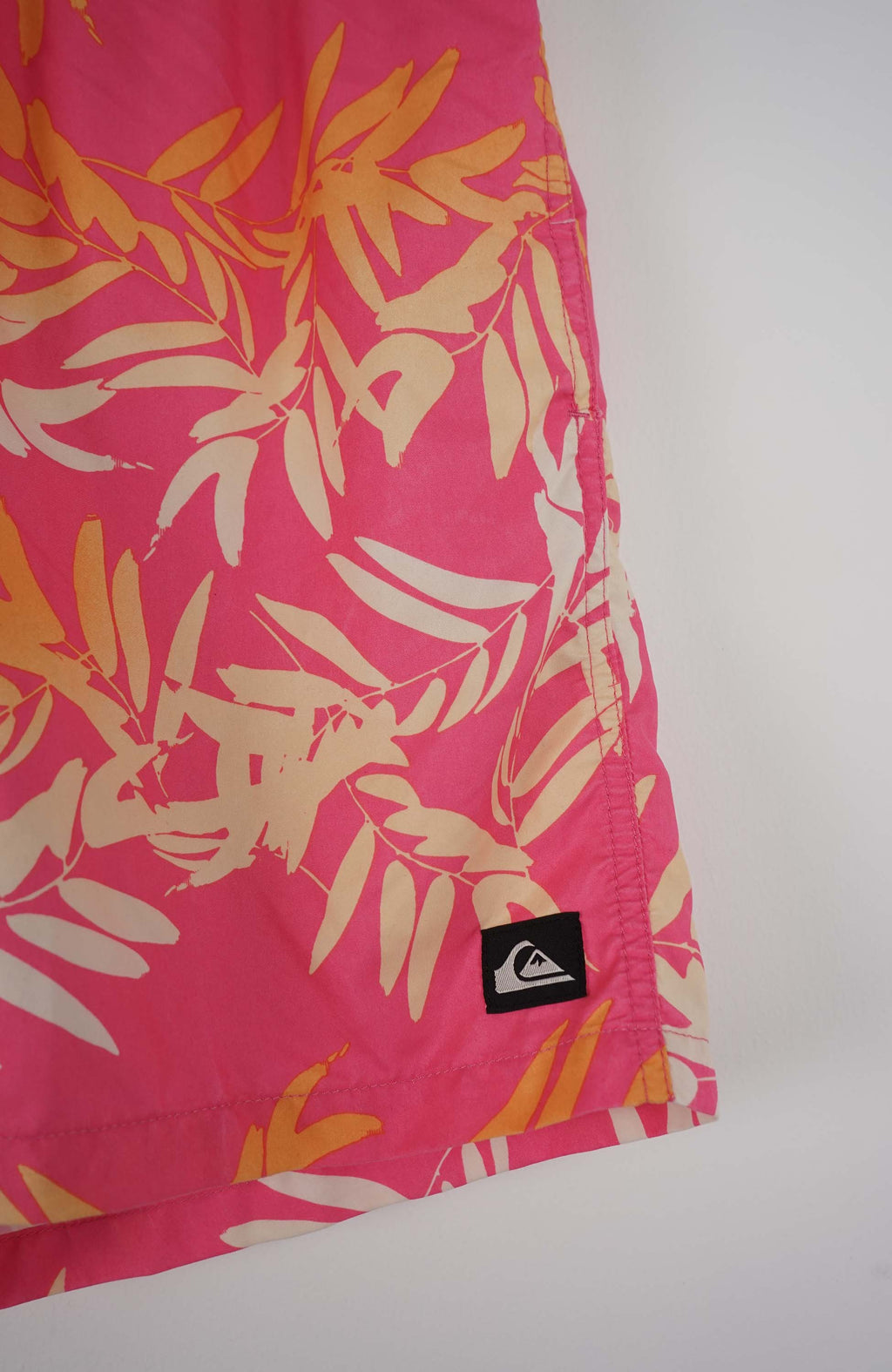 Pink swim shorts with tropical leaf pattern on a white background