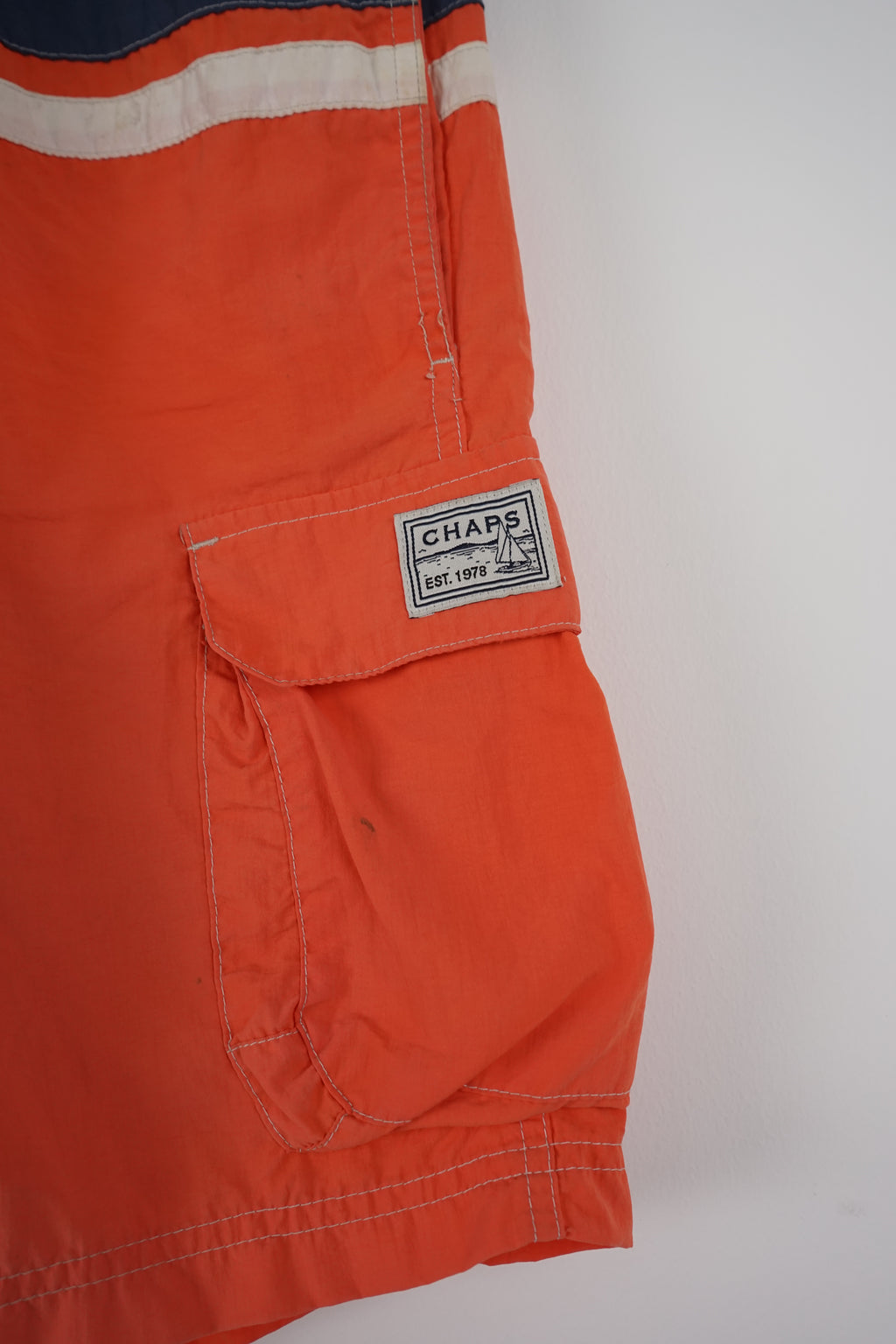 Orange shorts with blue and white stripes hanging on a white background
