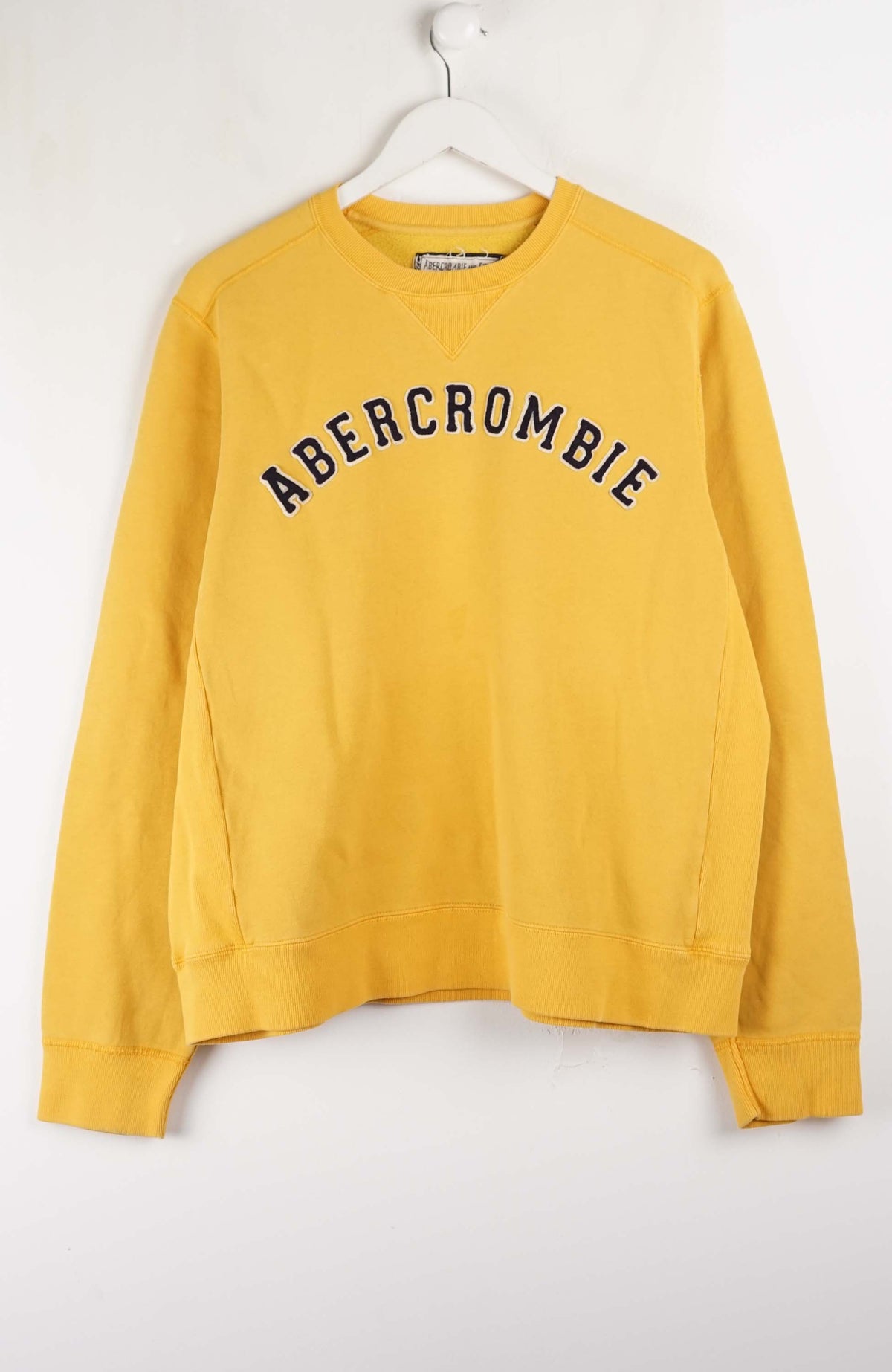 Yellow Abercrombie sweatshirt on a white hanger against a white background
