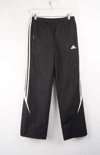 Black Adidas tracksuit pants with white stripes on a white background