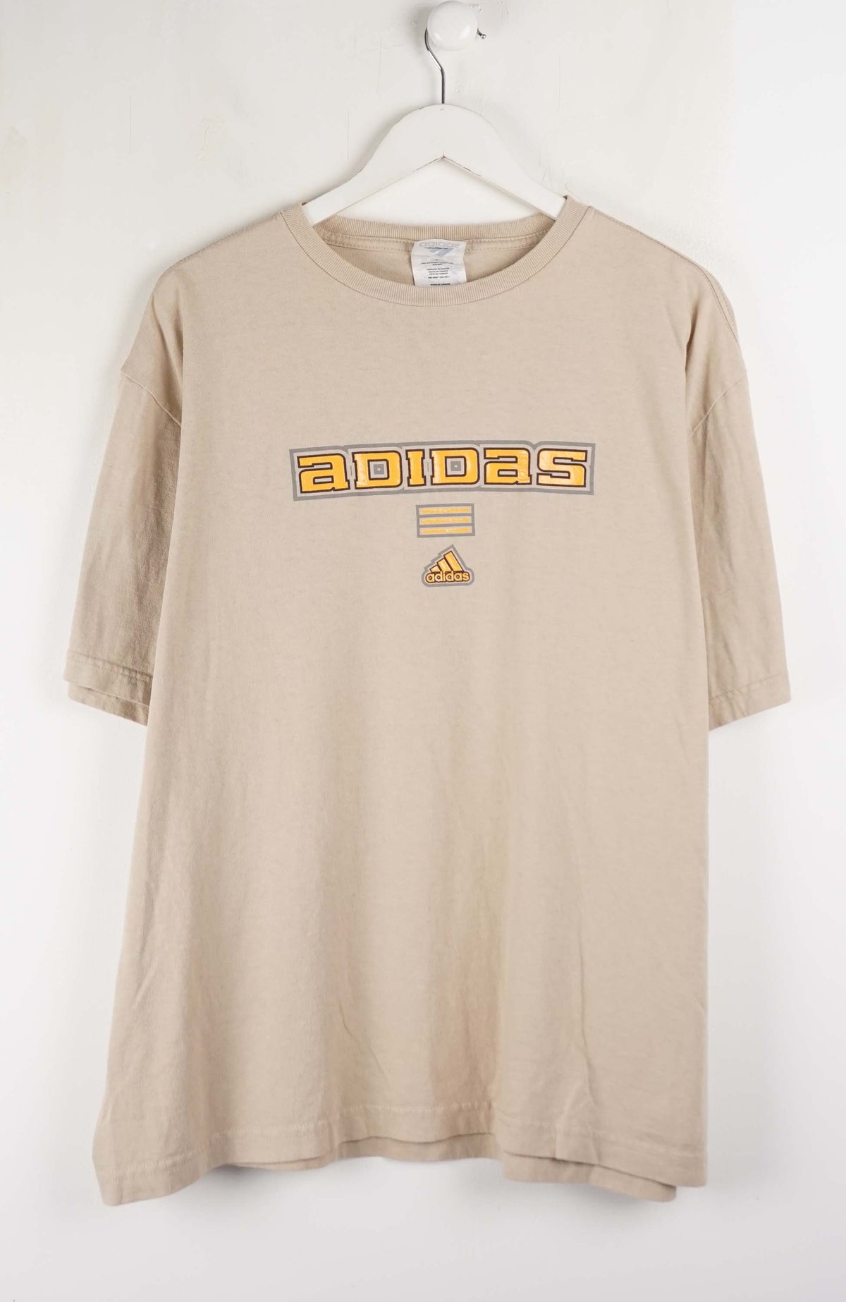 Beige Adidas t-shirt on a white hanger against a white background