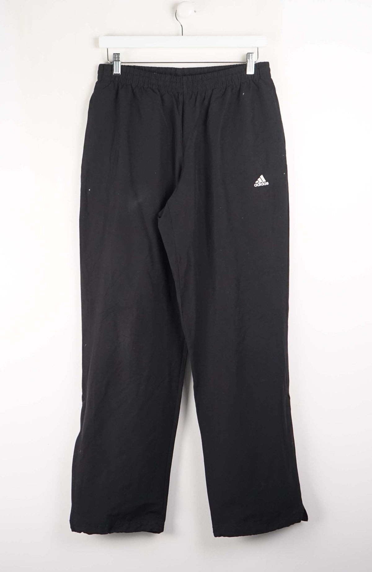 Black Adidas pants hanging on a white background