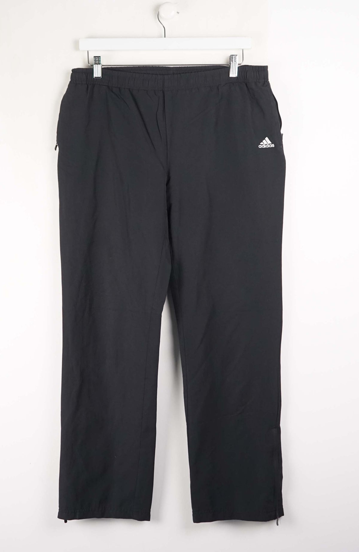Black Adidas pants on a white hanger against a white background