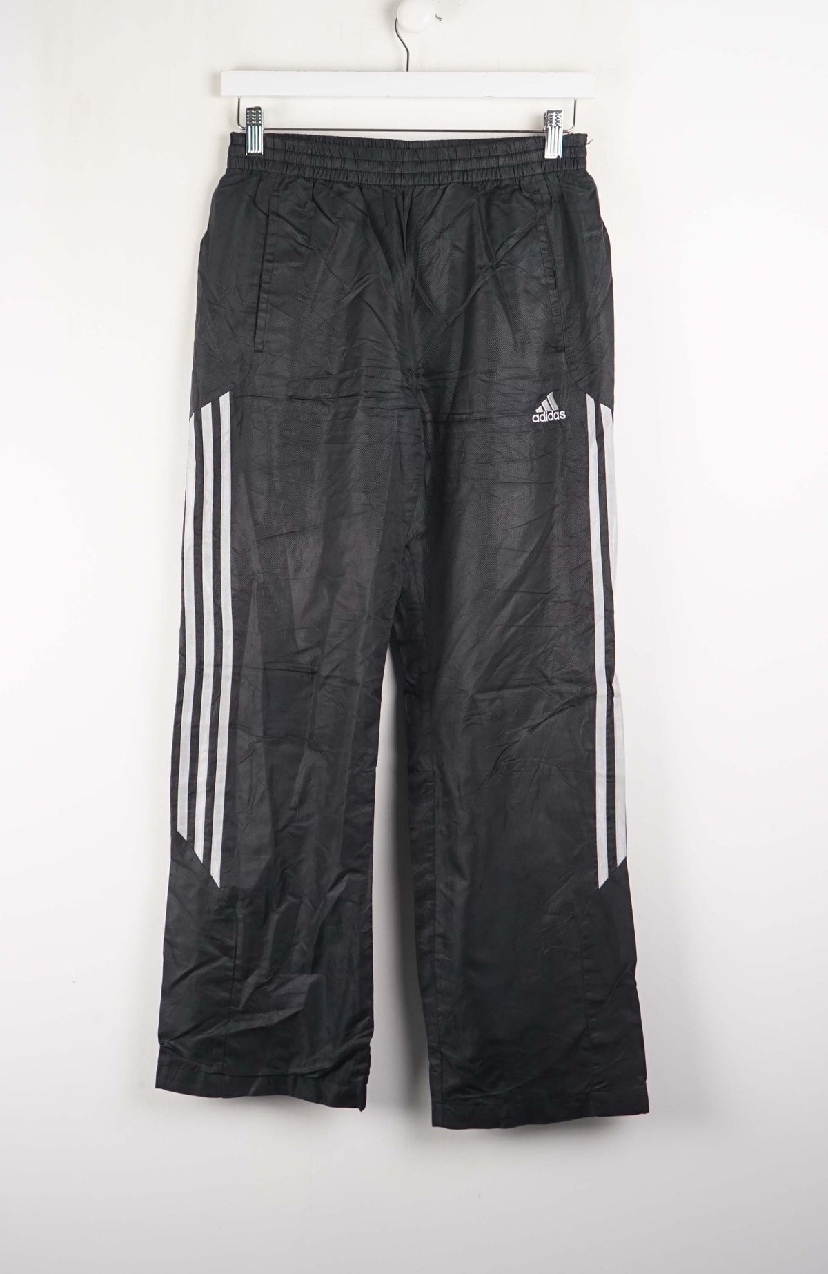 Black Adidas pants with white stripes hanging on a white background