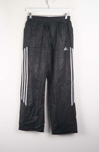Black Adidas pants with white stripes hanging on a white background