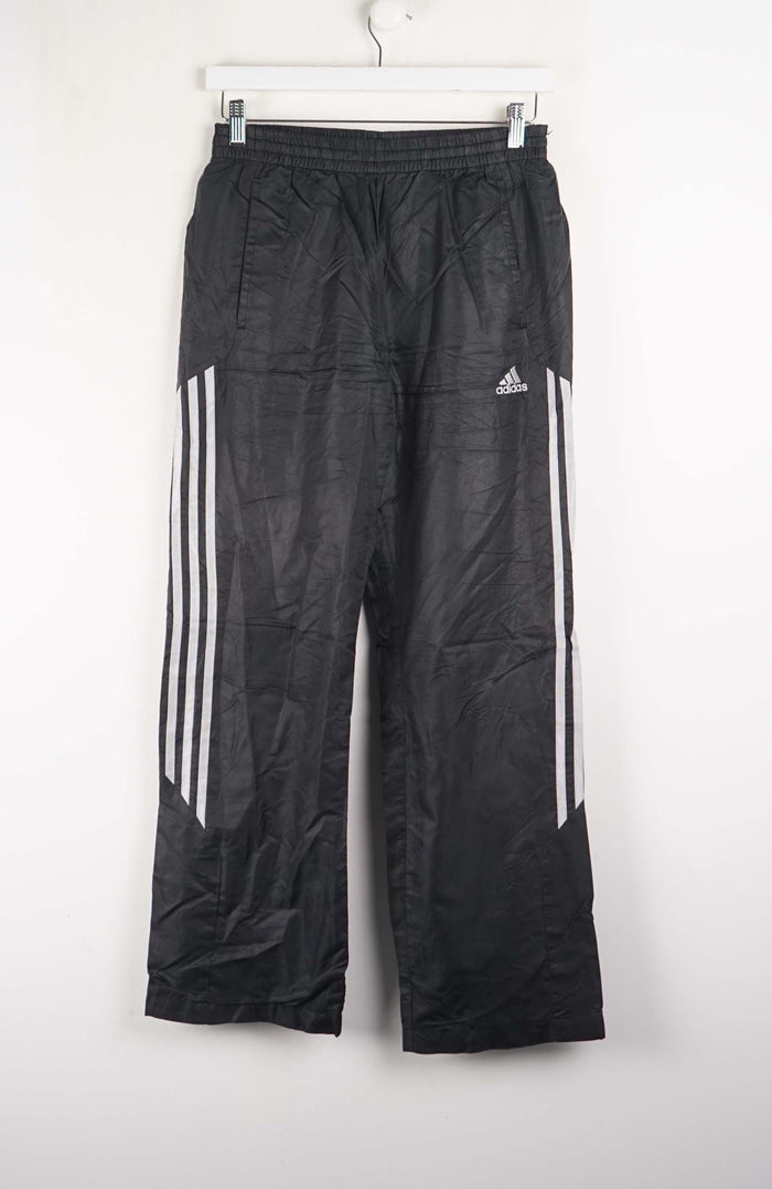 Black Adidas pants with white stripes hanging on a white background
