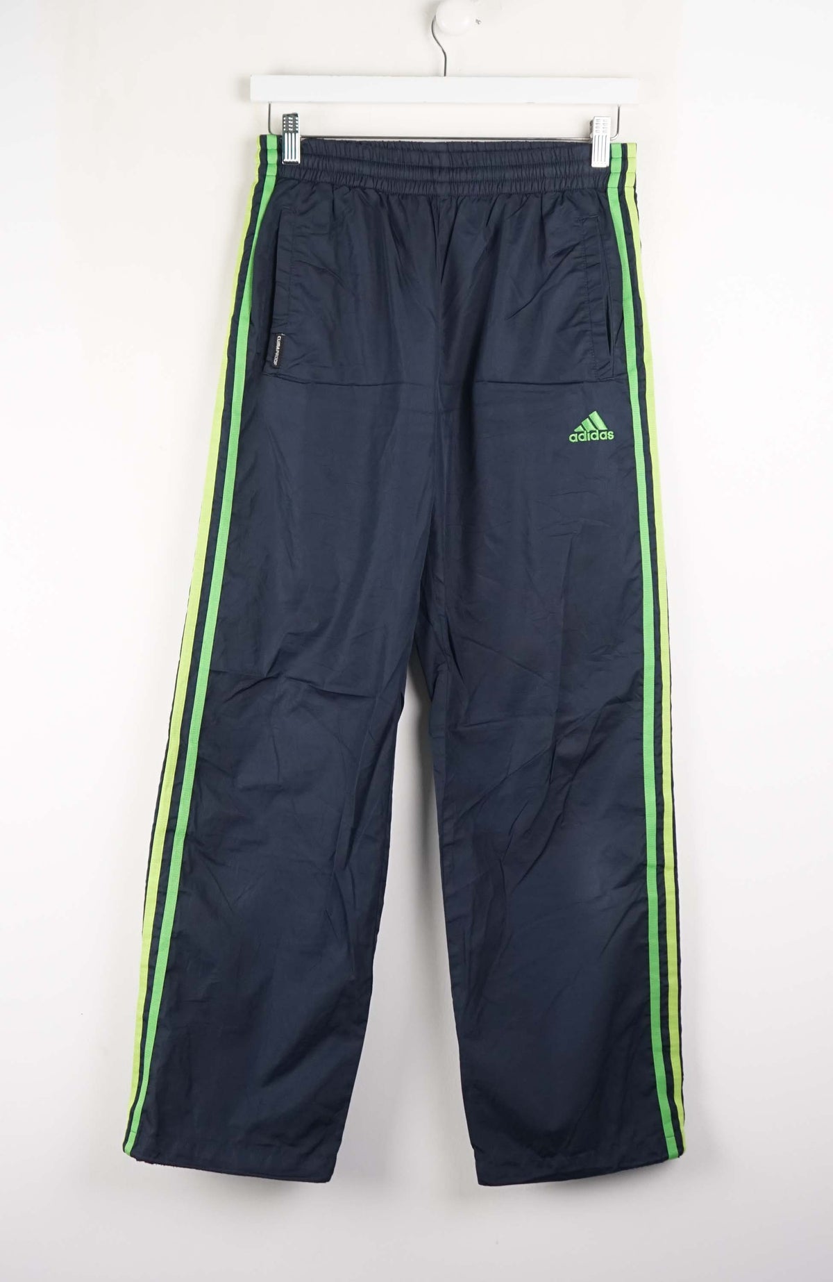 Navy blue tracksuit pants with green stripes and Adidas logo on a white background