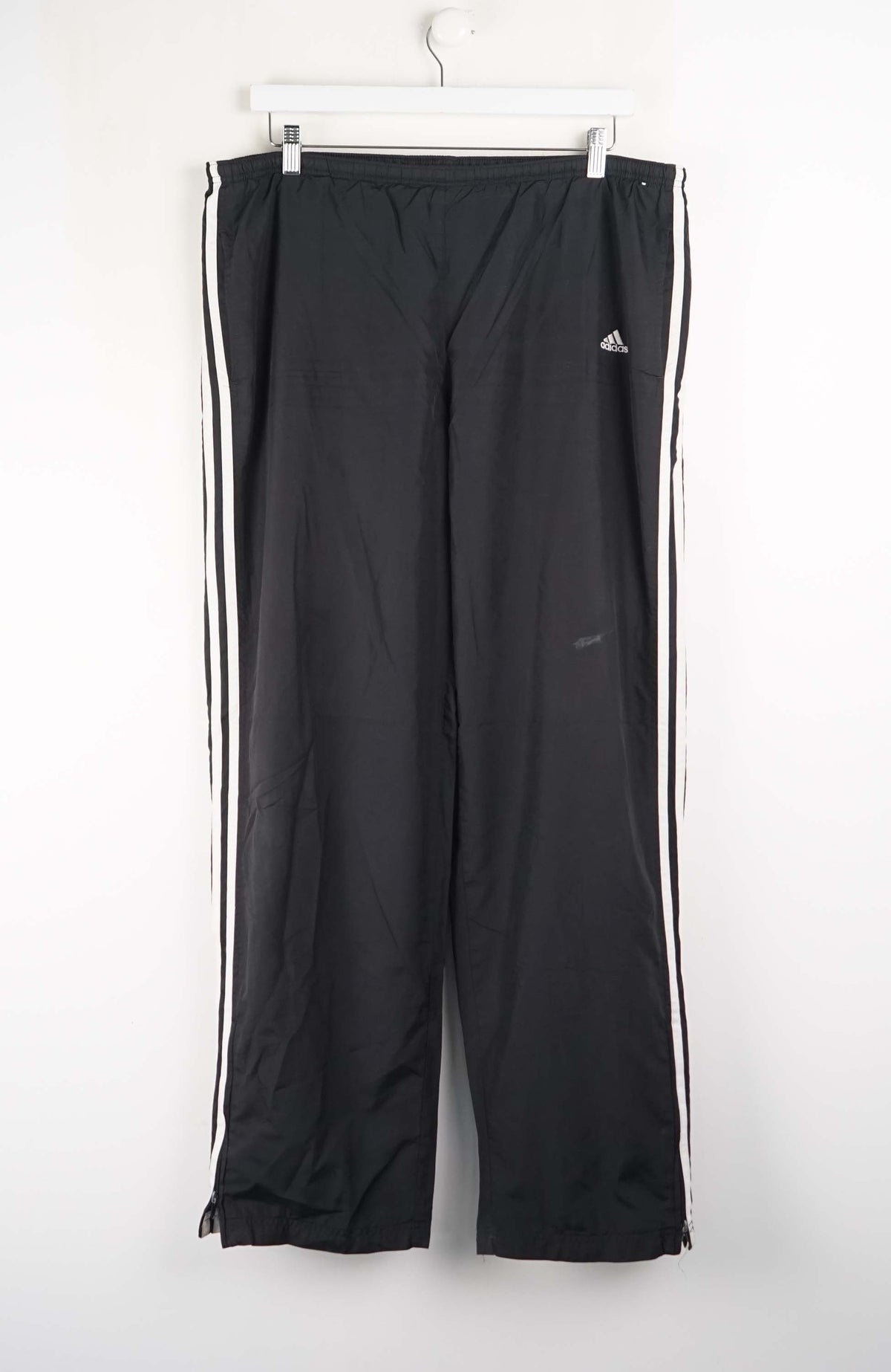 Black Adidas tracksuit pants with white stripes on a white background