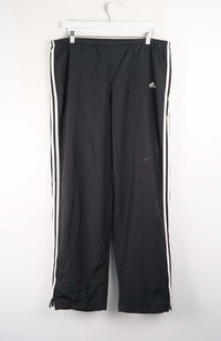 Black Adidas tracksuit pants with white stripes on a white background