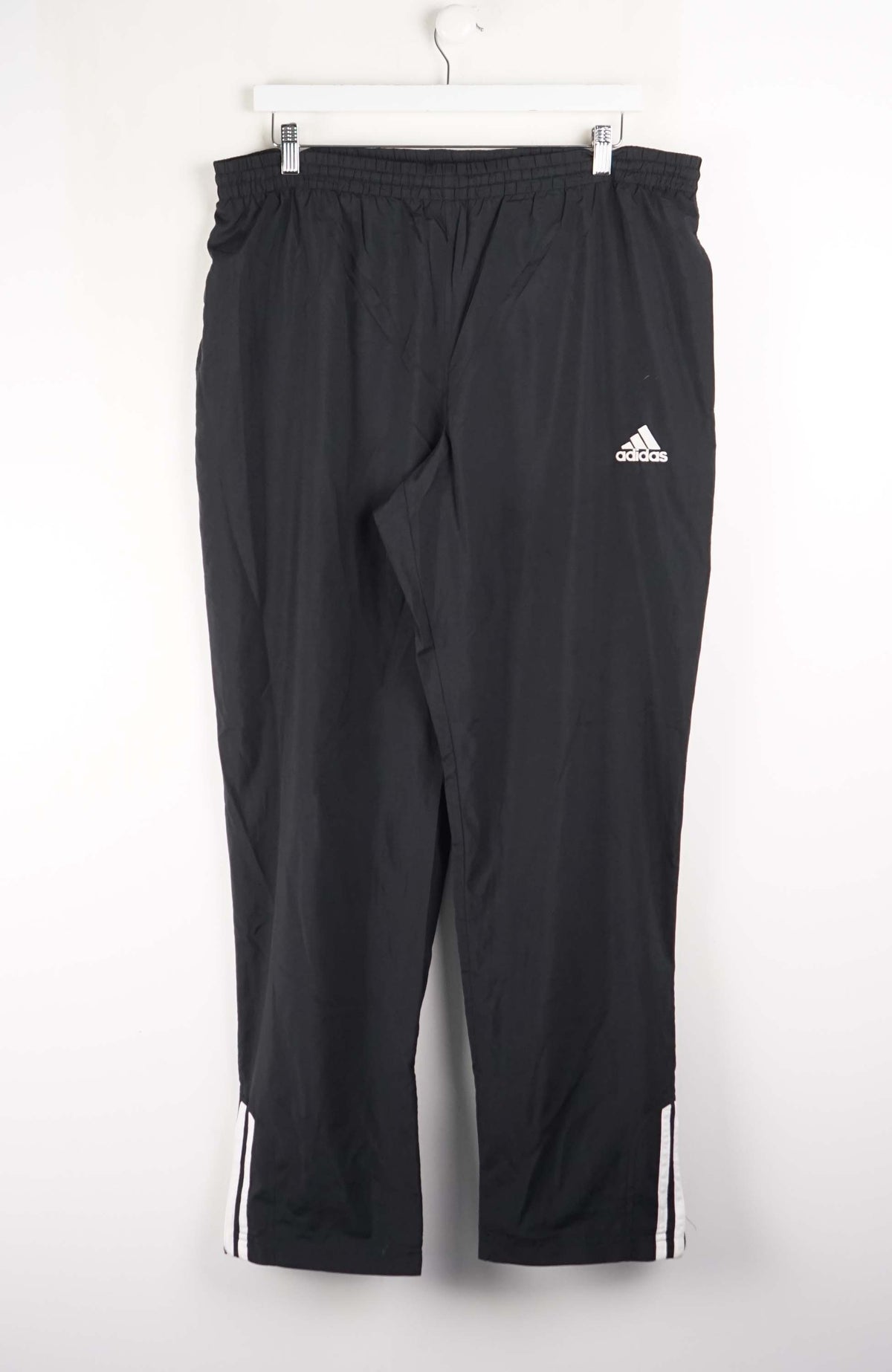 Black Adidas pants hanging on a white background