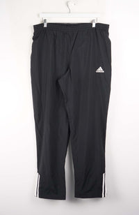 Black Adidas pants hanging on a white background