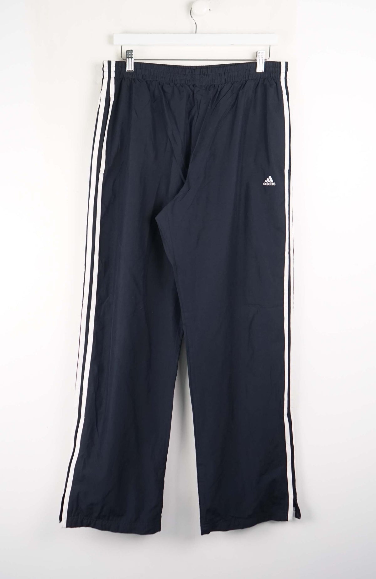 Navy blue Adidas tracksuit pants with white stripes on a white background