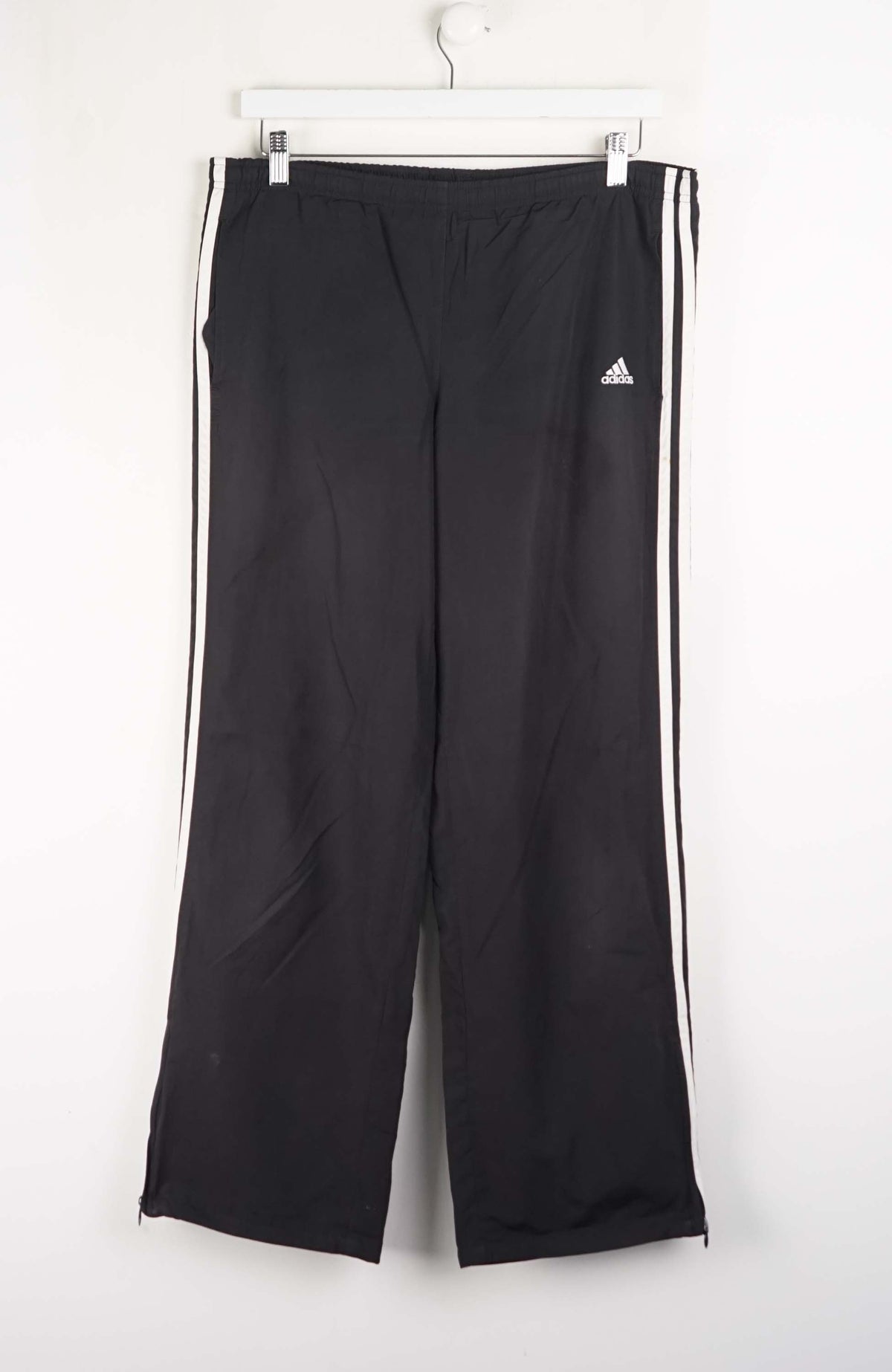 Black Adidas tracksuit pants with white stripes on a white background