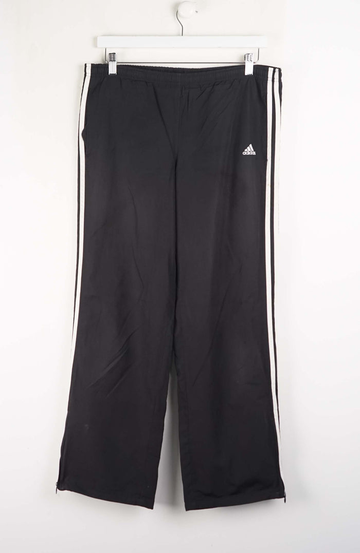 Black Adidas tracksuit pants with white stripes on a white background