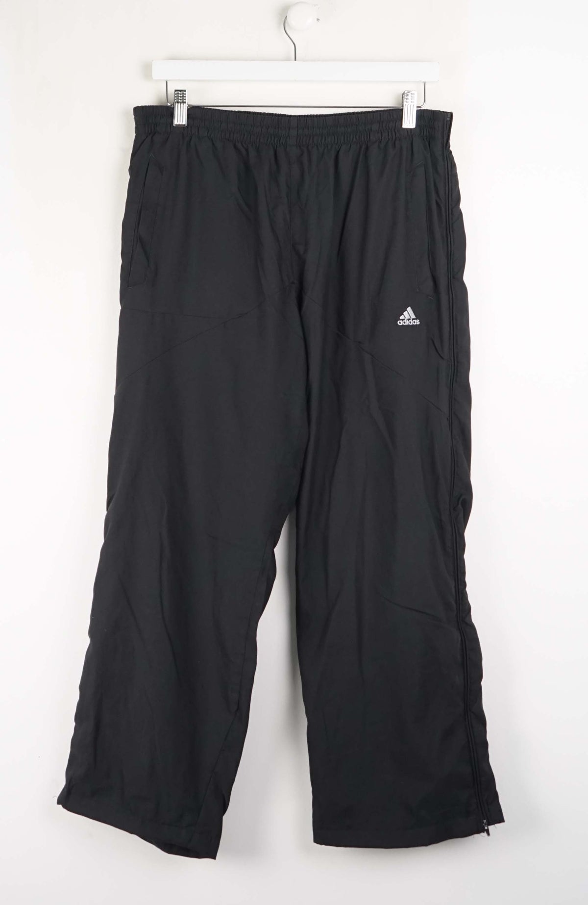 Black Adidas pants hanging on a white background