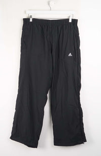 Black Adidas pants hanging on a white background