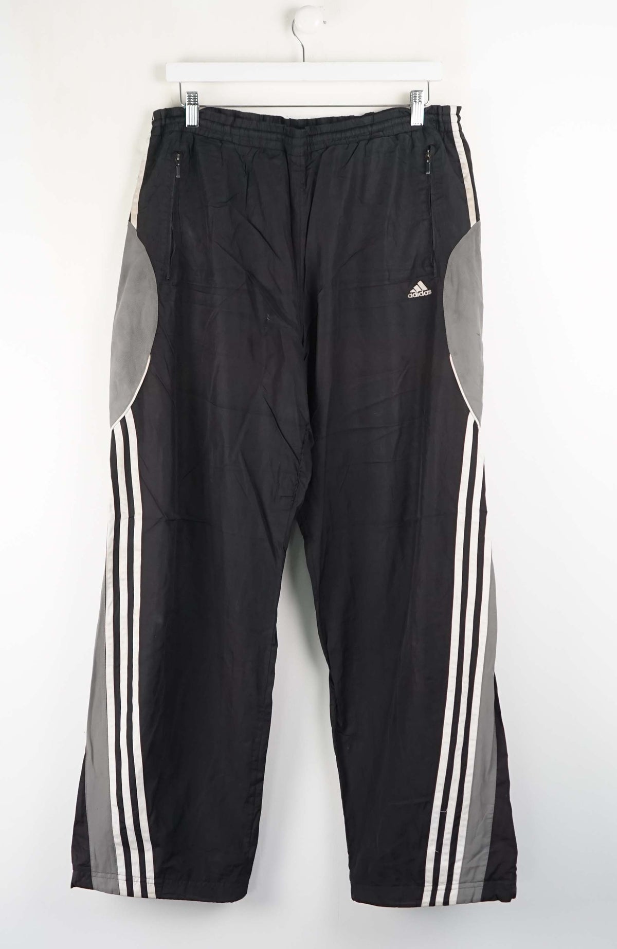 Black Adidas tracksuit pants with white stripes on a white background