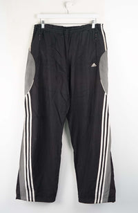 Black Adidas tracksuit pants with white stripes on a white background