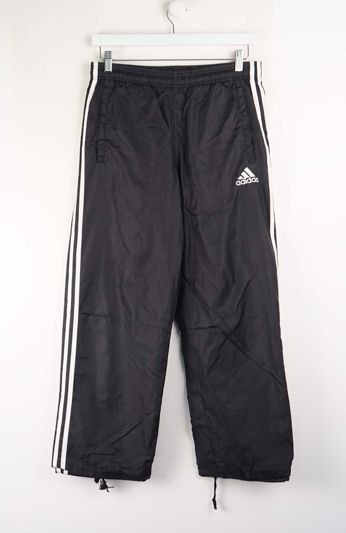 Black Adidas tracksuit pants with white stripes on a white background