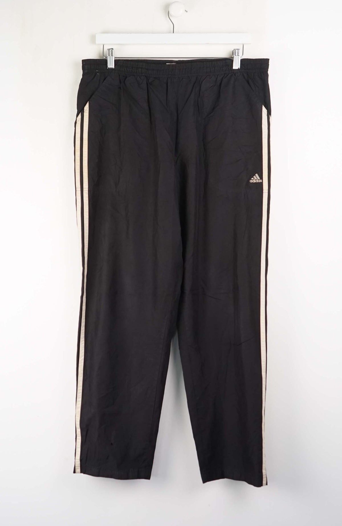 Black Adidas tracksuit pants with white stripes on a white background