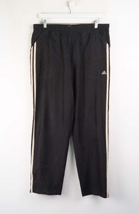Black Adidas tracksuit pants with white stripes on a white background