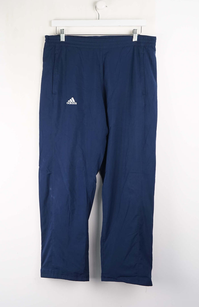 Navy blue Adidas pants hanging on a white rack against a white background
