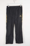 Black Adidas pants with gold stripes on a white background