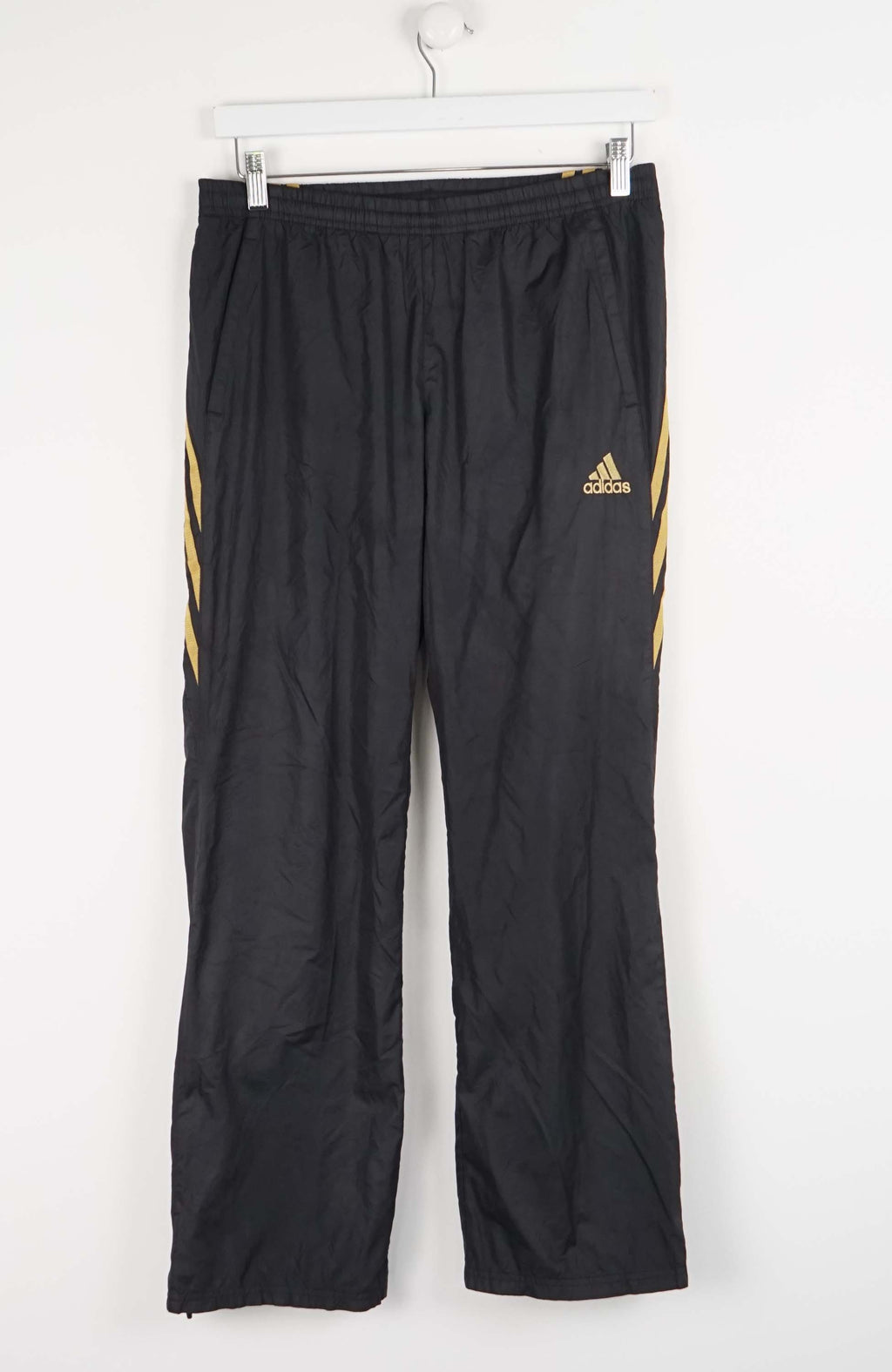 Black Adidas pants with gold stripes on a white background