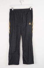 Black Adidas pants with gold stripes on a white background