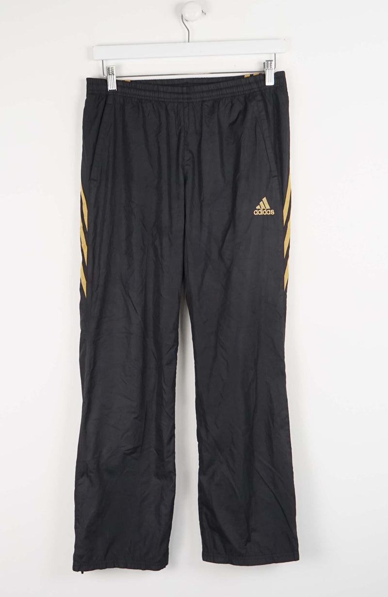Black Adidas pants with gold stripes on a white background
