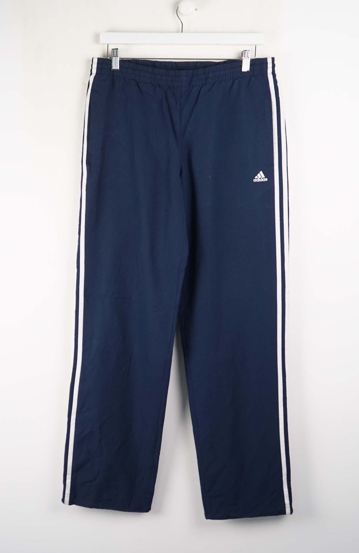Navy blue Adidas tracksuit pants with white stripes on a white background