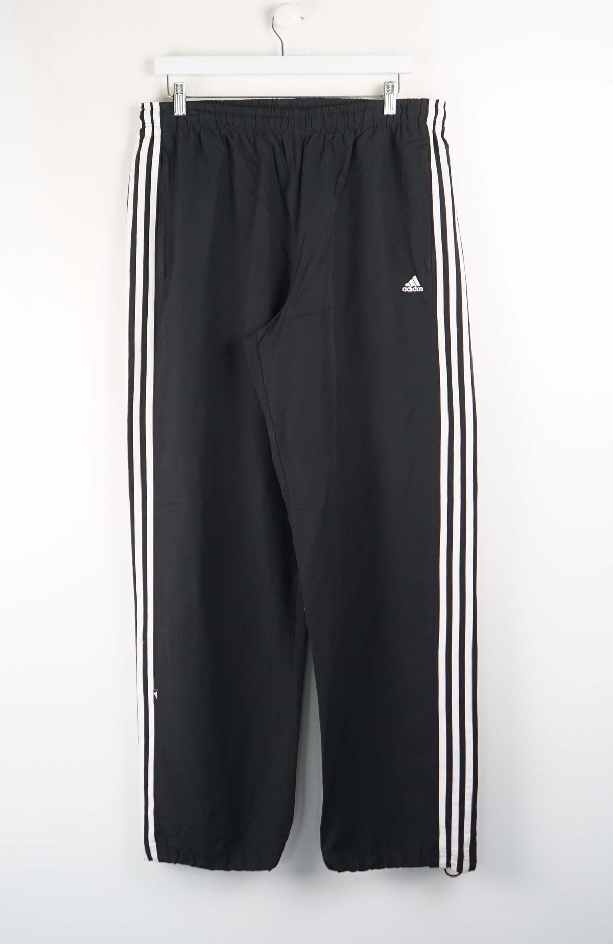 Black Adidas tracksuit pants with three white stripes on a white background