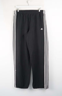 Black Adidas tracksuit pants with three white stripes on a white background