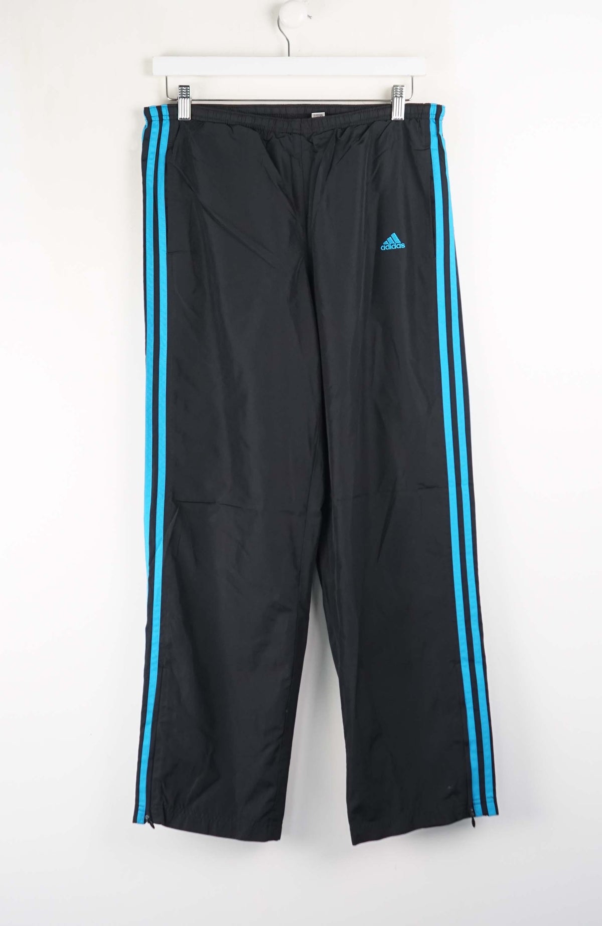 Black Adidas tracksuit pants with blue stripes on a white background