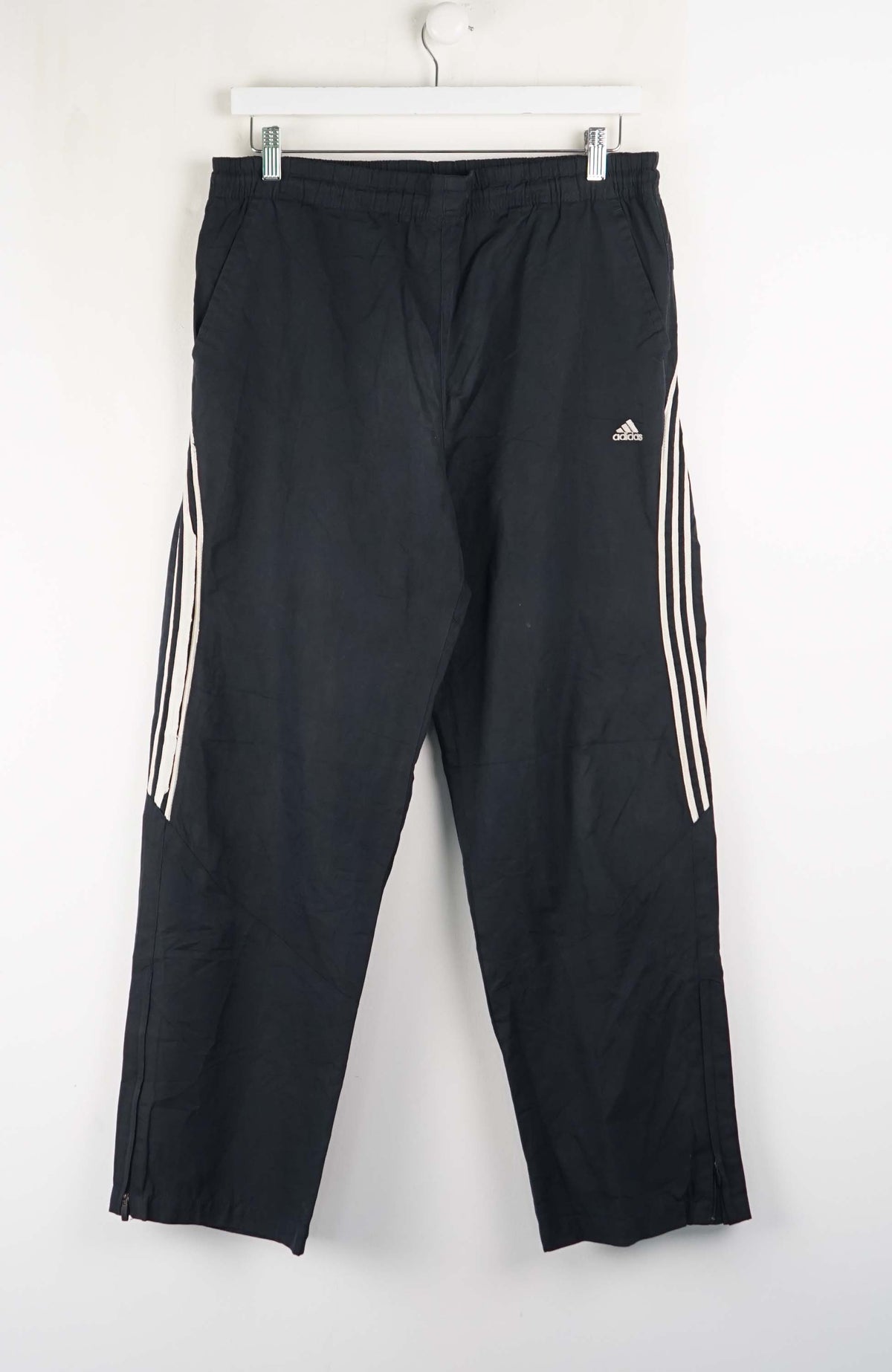 Black Adidas tracksuit pants with three white stripes on a white background