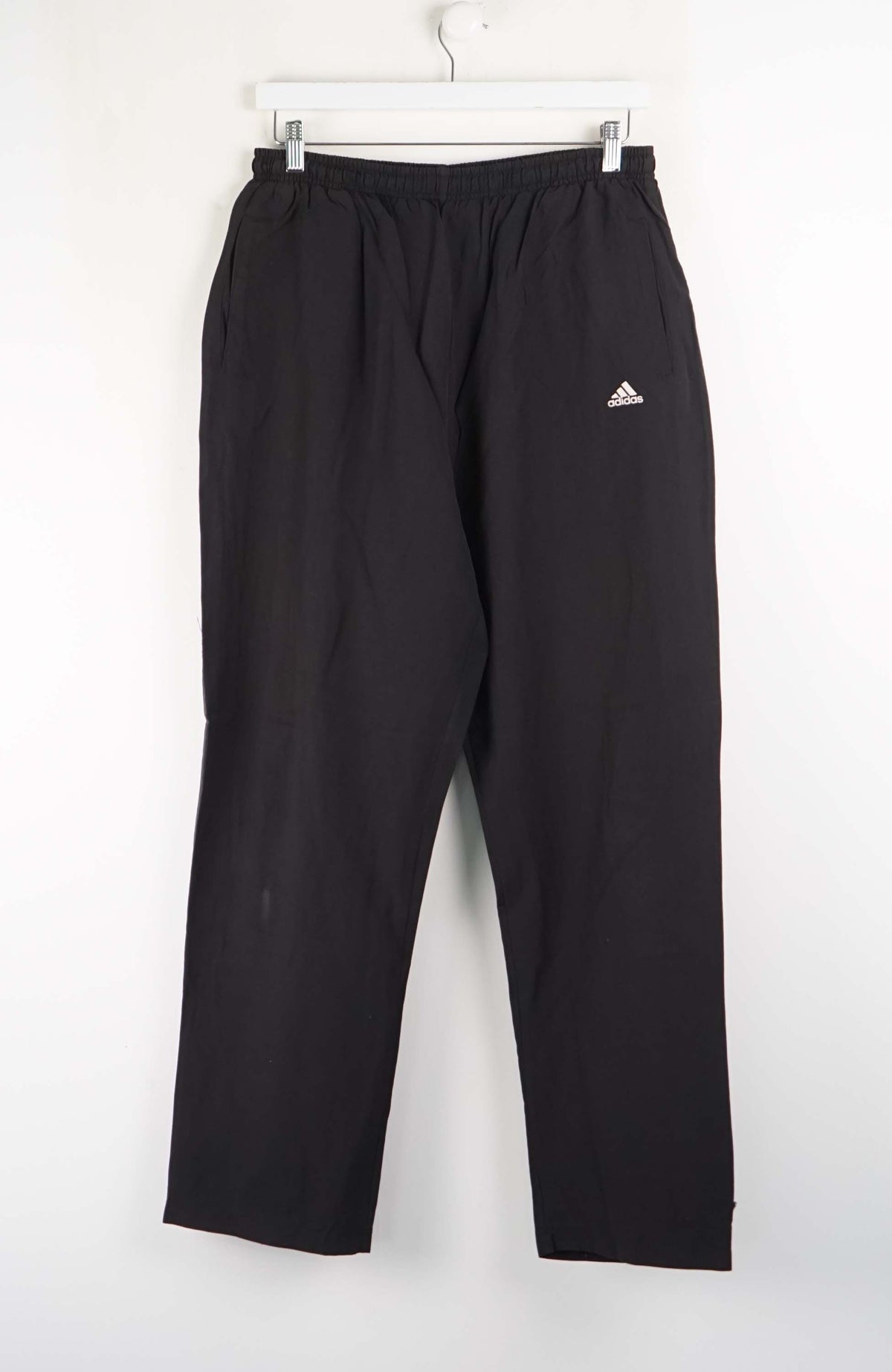 Black Adidas pants hanging on a white background