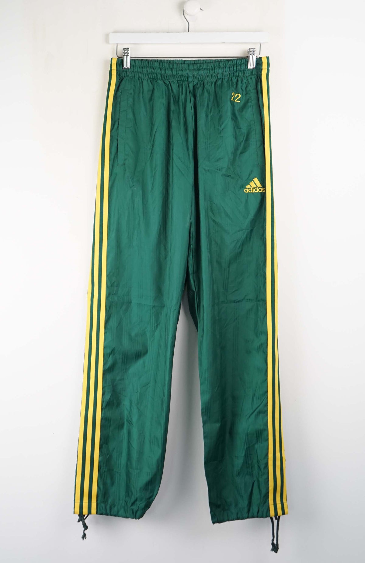 Green Adidas tracksuit pants with yellow stripes on a white background