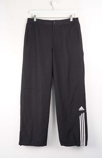 Black Adidas pants hanging on a white background