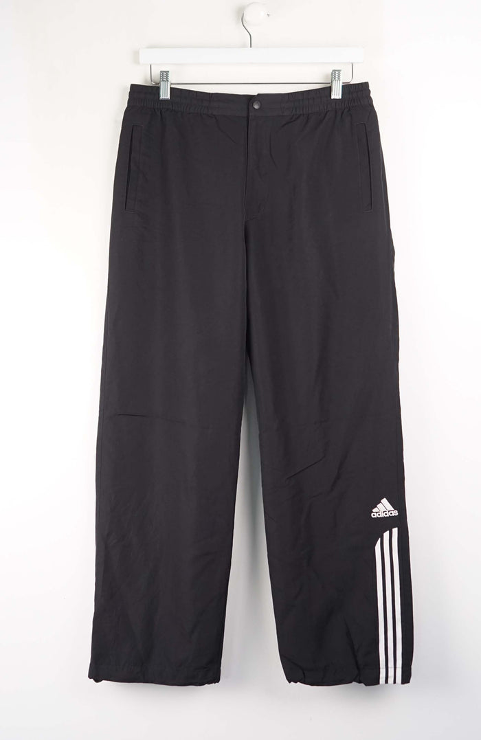 Black Adidas pants hanging on a white background