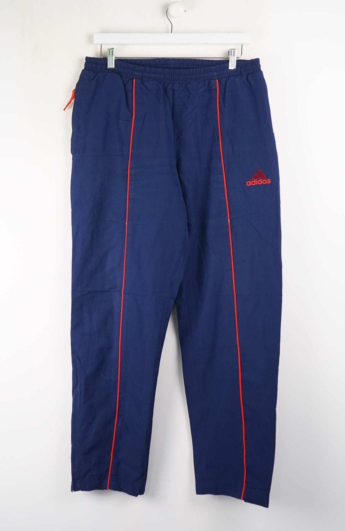 Blue tracksuit pants with red accents and Adidas logo on a white background