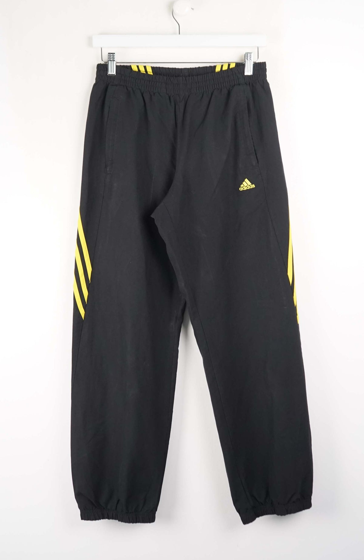 Black Adidas tracksuit pants with yellow stripes on a white background
