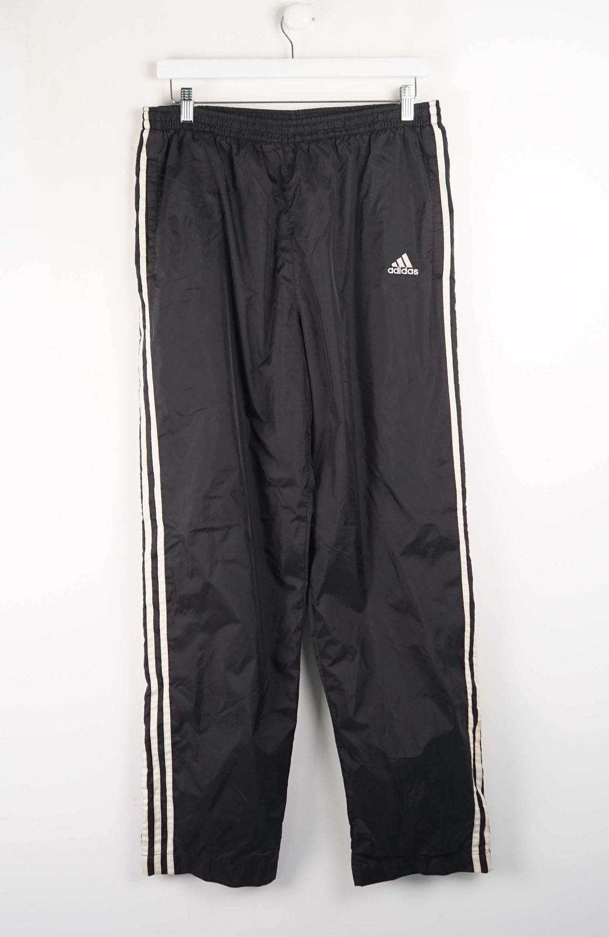 Black Adidas tracksuit pants with white stripes on a white background