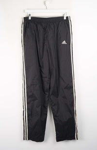 Black Adidas tracksuit pants with white stripes on a white background