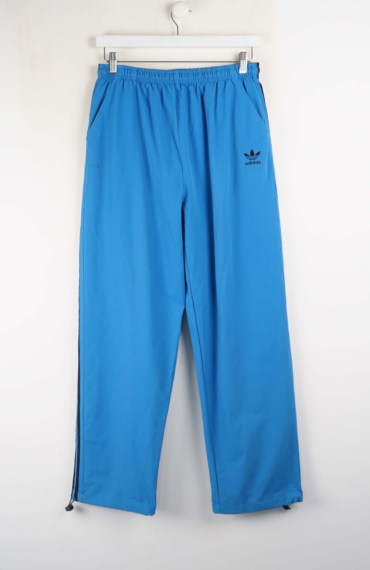 Blue Adidas pants hanging on a white background