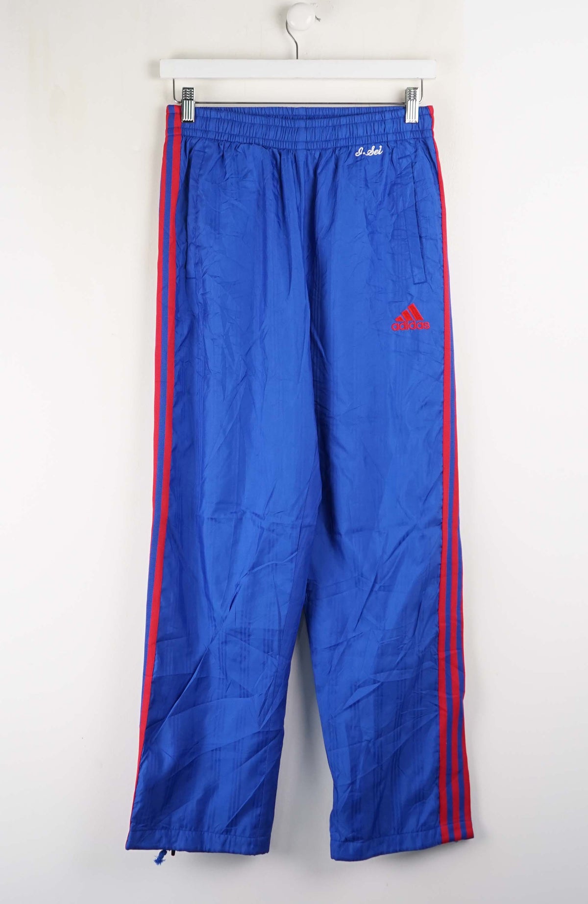 Blue tracksuit pants with red stripes and Adidas logo on a white background