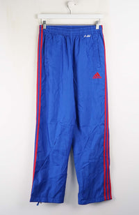 Blue tracksuit pants with red stripes and Adidas logo on a white background